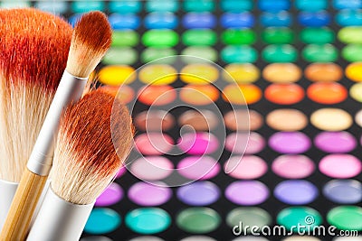 Makeup brushes and set of colorful eye shadows as background