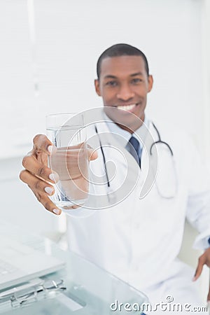 Male doctor holding out a glass of water in medical office
