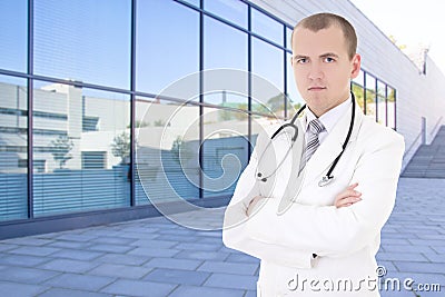 Male doctor standing on street against modern hospital building