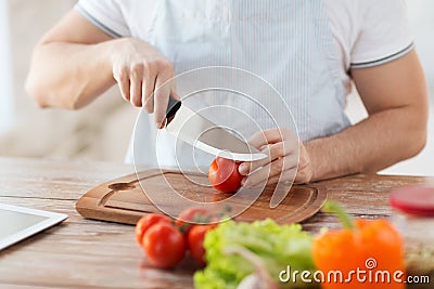 Male hand cutting tomato on board with knife