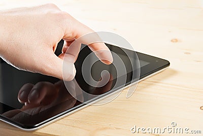 Male hand is touching digital tablet pc on wood table