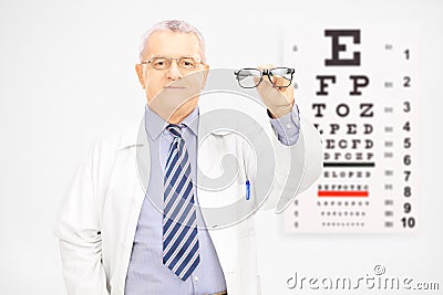 Male optician holding glasses in front of an eye chart