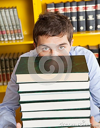 Male Student Peeking Over Stacked Books In Library