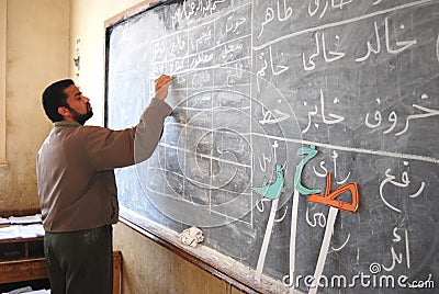 Male teacher in class room writing arabic on the blackboard