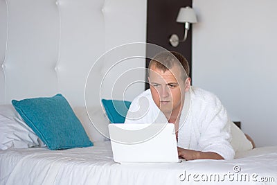 Man in bathrobe with laptop in hotel room