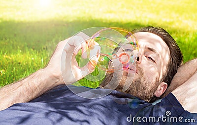 Man blowing soap bubbles while laying outdoor on grass