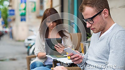 Man with cell phone and the woman with the iPad sitting in a café.