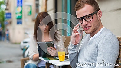 Man with cell phone and the woman with the iPad sitting in a cafe.
