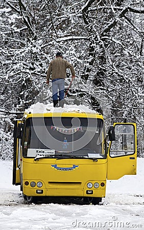 The man cleans snow from a bus roof after snowfall