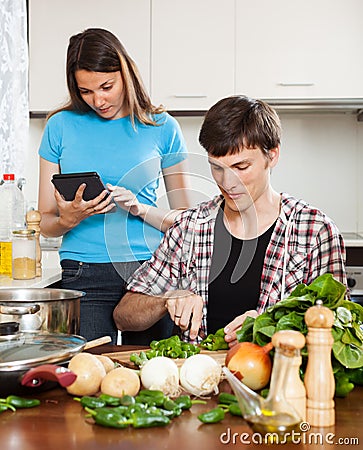 Man cooking food while woman reading eBook