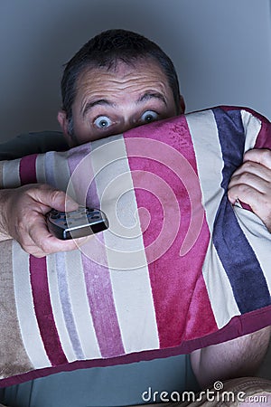 Man covering face with a cushion watching tv