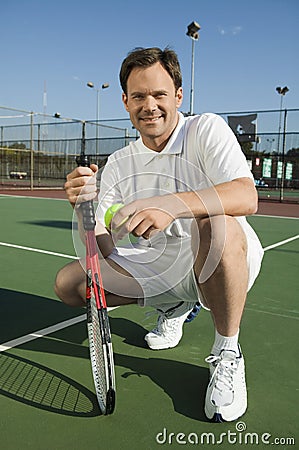 Man crouching on Tennis Court holding tennis racket and ball portrait