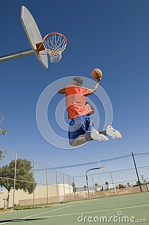Man Dunking Basketball Into Hoop Against Blue Sky