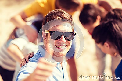 Man with friends on the beach showing thumbs up
