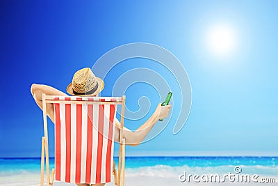 Man with hat sitting on a beach chair and holding a beer next to