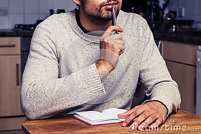 Man in kitchen is thinking and writing