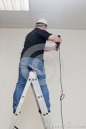 Man on a ladder drills drill