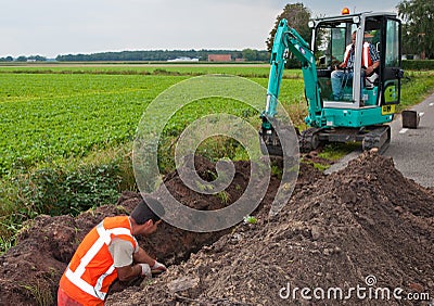 Man and mini excavator dig a trench to lay cables