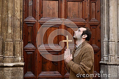 Man praying in front of the church holding a cross