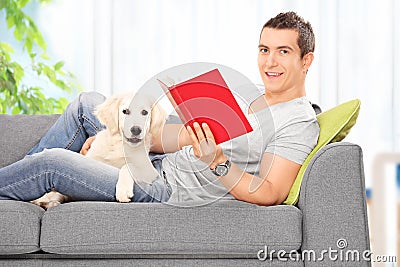 Man reading book and lying on sofa with a dog