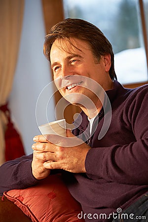 Man Relaxing With Hot Drink On Sofa Watching TV