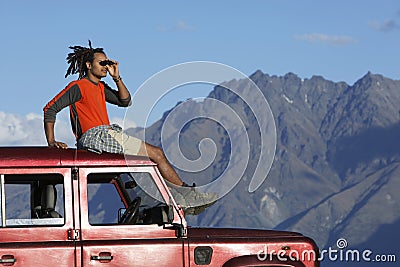 Man Shading Eyes On Top Of Jeep Near Mountains