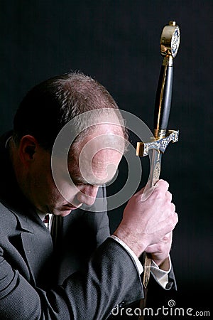 Man in a suit kneeling and gripping a sword