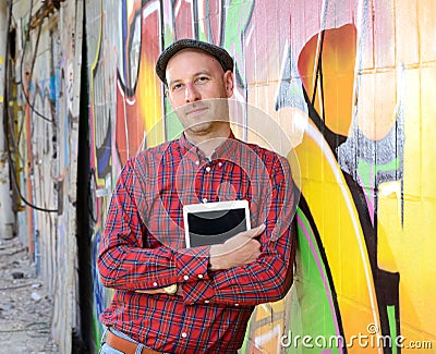 Man with tablet PC is leaning against a graffiti- wall