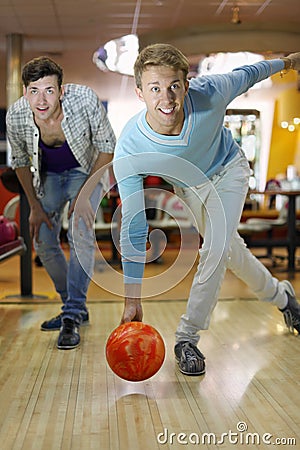 Man throws ball in bowling; friend looks at aim