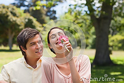 Man watching his friend while she is smelling a flower