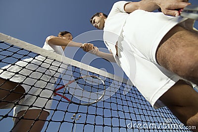 Man and woman shaking hands over tennis net on court view from below