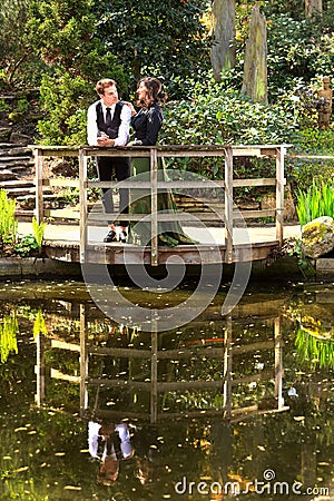 Man and woman in Victorian fashion near lake with reflections in park