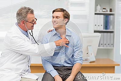 Mature doctor listening to his happy patients chest with stethoscope