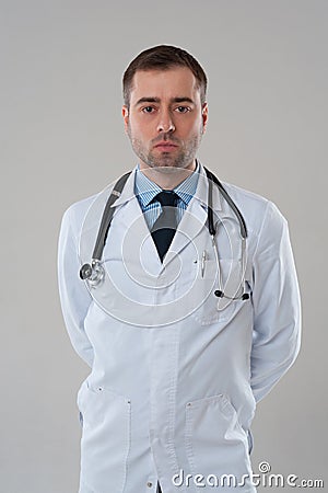 Mature male doctor with serious face standing on grey background