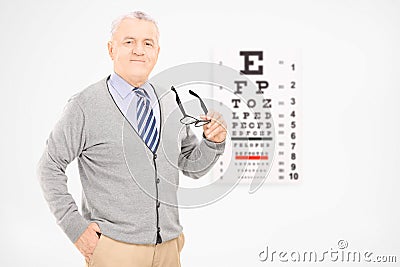 Mature man holding a pair of glasses in front of an eye chart