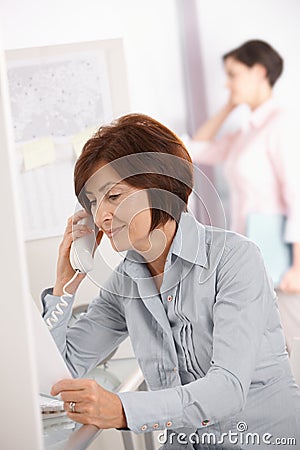 Mature office worker woman using landline phone