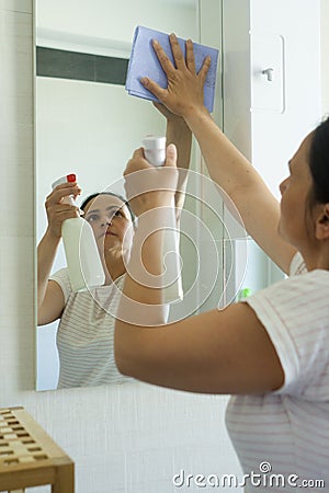 Mature woman with cleaning spray and cloth in bathroom