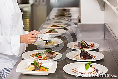 Mid section of a female chef garnishing food in kitchen