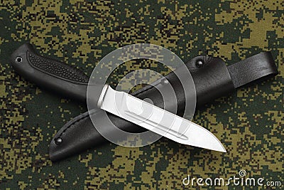 Military knife lying across black leather sheath on camouflage background