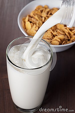 Milk pouring into glass and bowl with cornflakes
