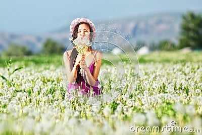 Model in a pink dress on a dandelion field in a straw hat