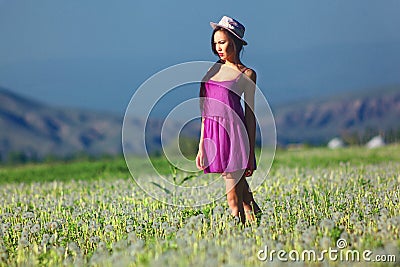 Model in a pink dress on a dandelion field in a straw hat