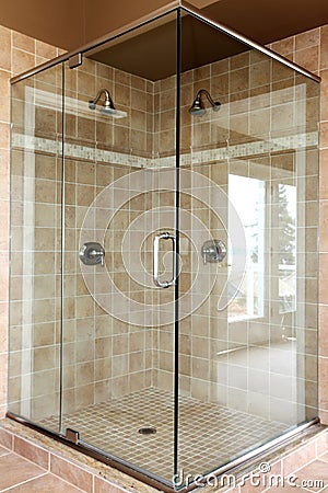 Modern new glass walk in shower with beige tiles.