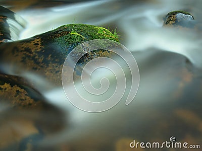 Mossy stone in blurred blue waves of mountain stream. Cold water is running and turning between boulders and bubbles create tr