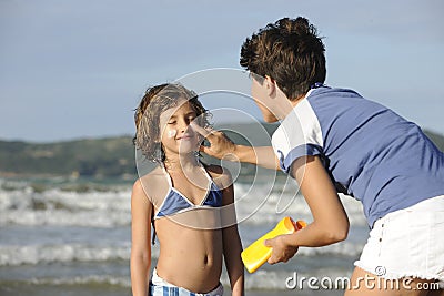 Mother applying sunscreen to daughter at beach.