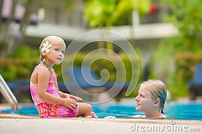 Mother and daughter with flower behind ear have fun at pool side