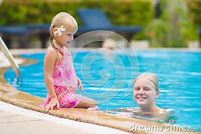 Mother and daughter with flower behind ear have fun at pool side