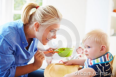 Mother Feeding Baby Boy In High Chair