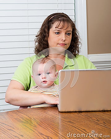 Mother holding baby while working on computer