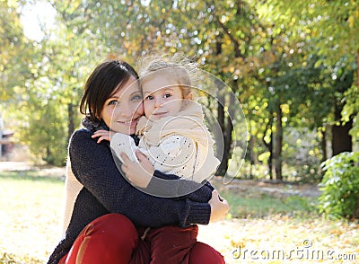 Mother hugging baby daughter in autumn park